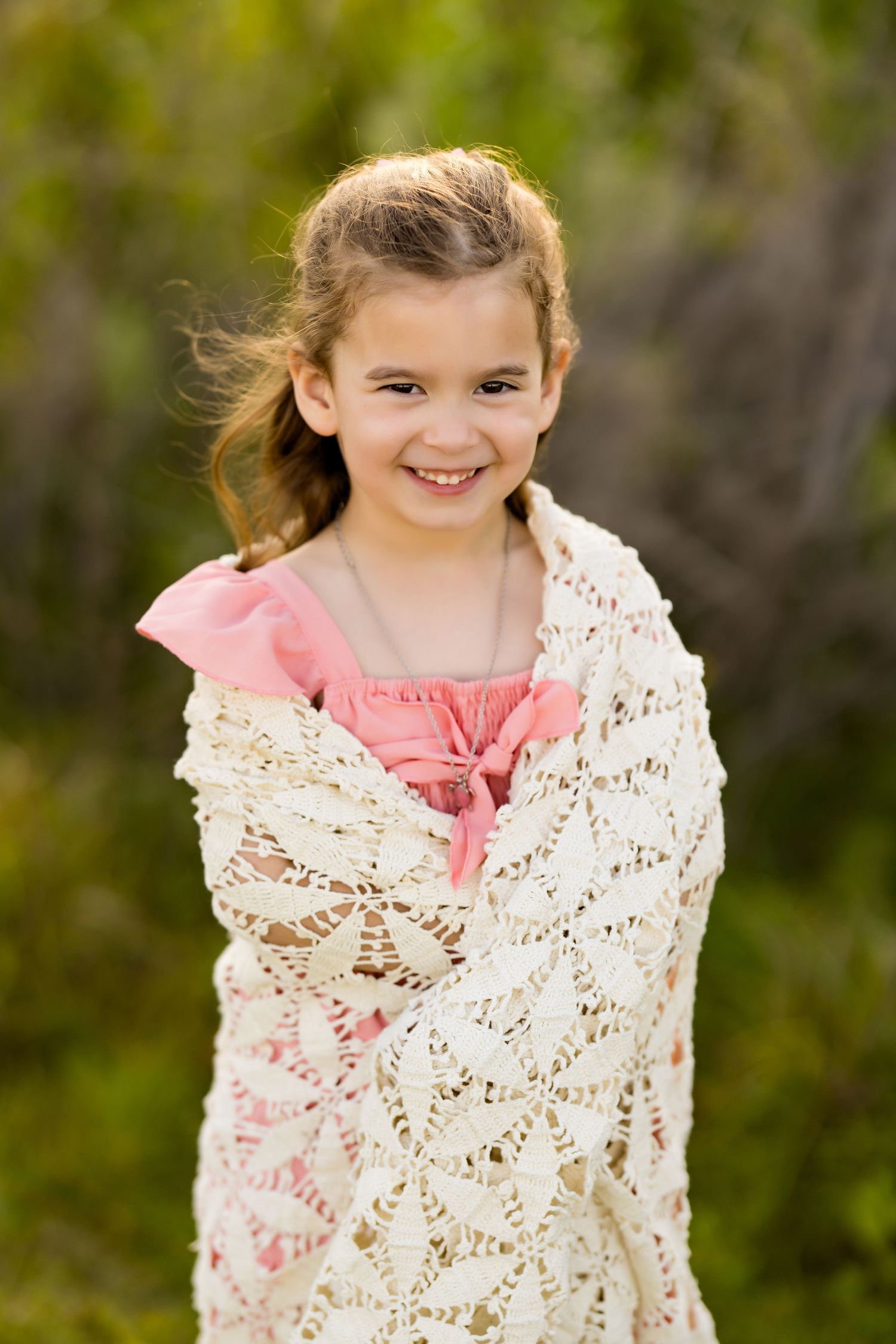 Wrapped in delicate white lace shawl over pink dress against natural foliage.