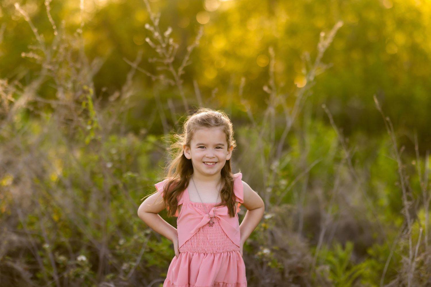 A sweet pink dress stands out against a golden sunset backdrop in a natural outdoor setting.