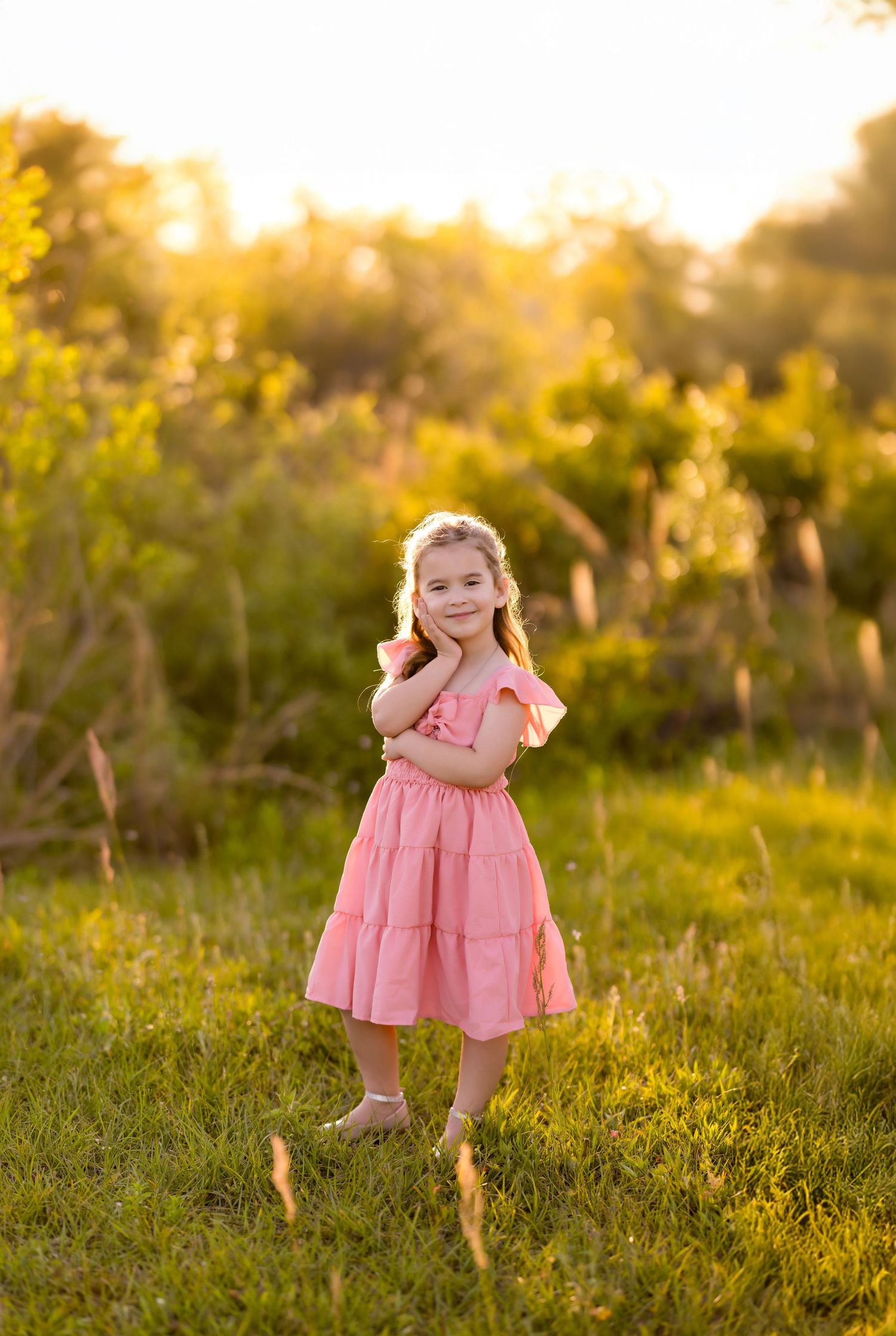 Pink ruffled dress twirls in golden evening light amid wild grasses.
