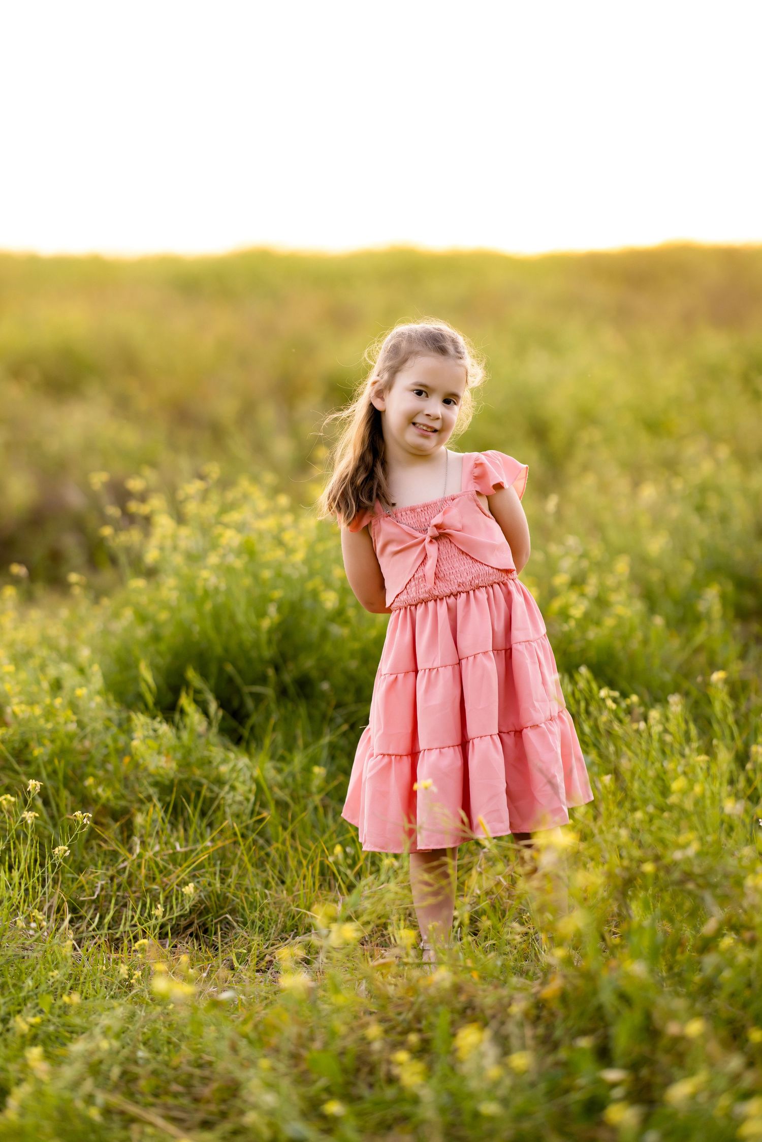 Coral pink tiered dress glows in late afternoon sunlight among wildflowers.