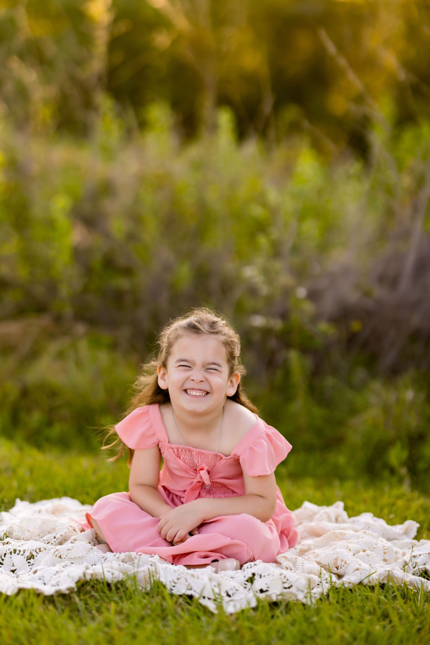 Relaxing on a white lace blanket in a pink dress amid natural greenery.