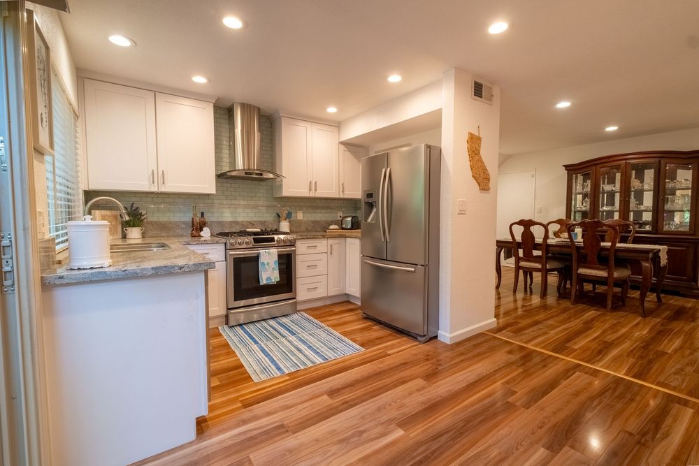 Modern white kitchen with hardwood floors, stainless appliances, and dining room view showcasing open-concept design.