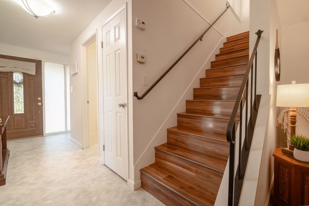 Bright entryway with wooden staircase, white walls, and tiled floor leading to a front door with sidelights.