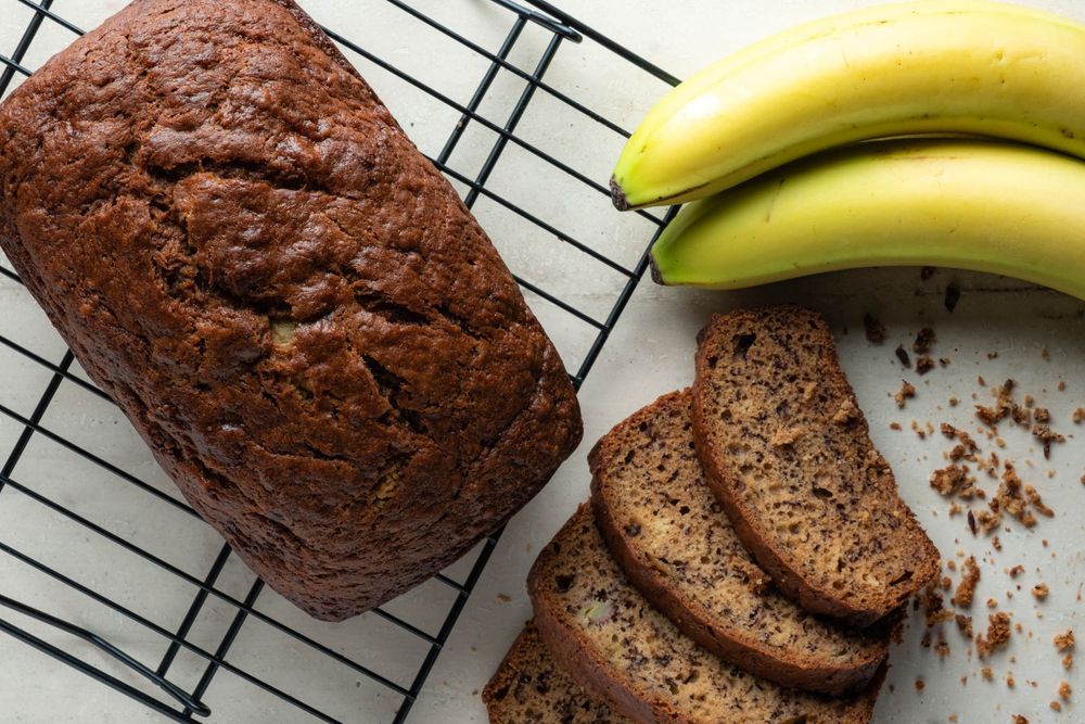 Freshly baked chocolate banana bread on cooling rack with fresh bananas.