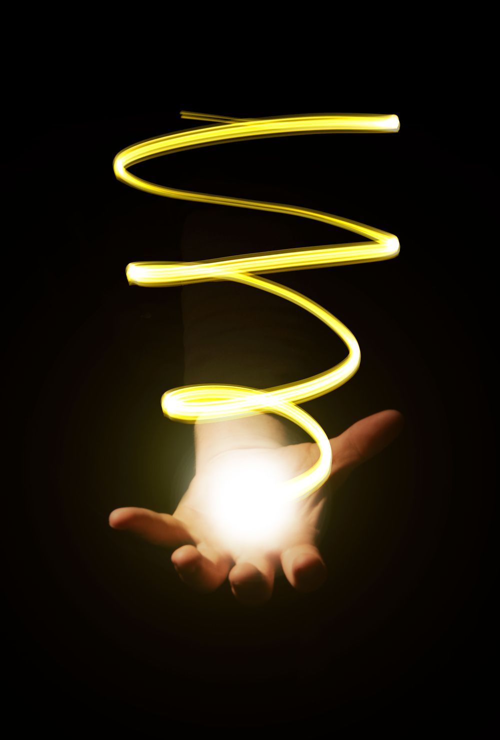 Spiral of glowing yellow light floating above outstretched hands in darkness.