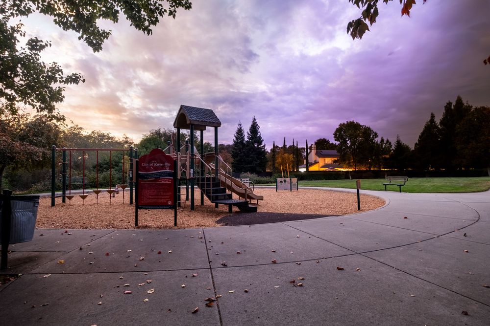 Empty playground at sunset with purple sky and red playground equipment.