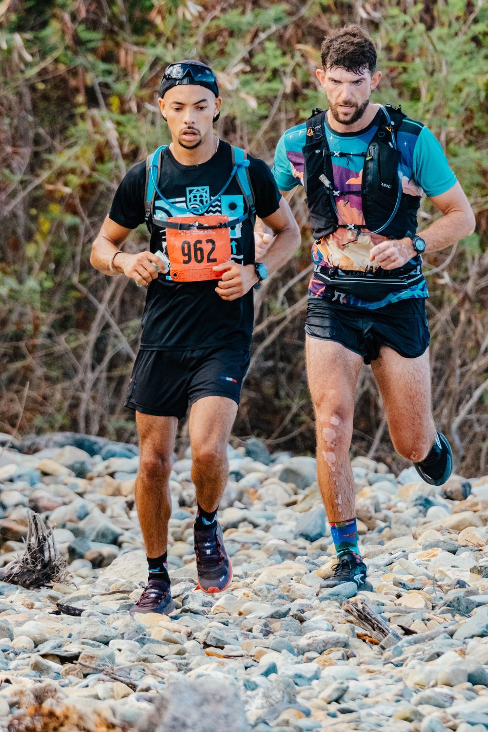 Two trail runners navigating rocky terrain during an endurance race, with one wearing race number 962.
