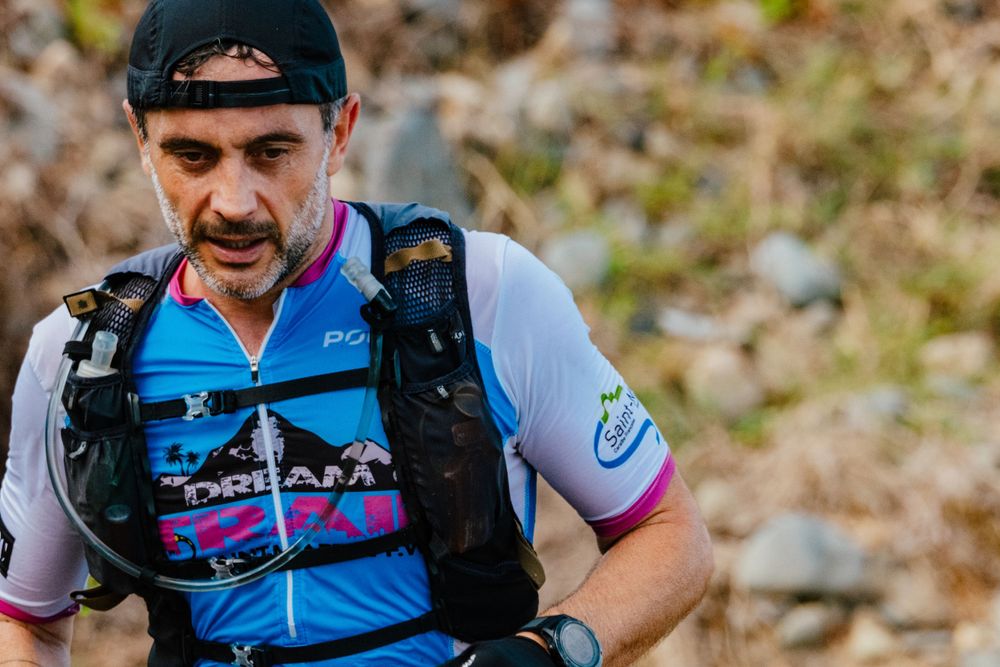 Trail runner wearing blue cycling jersey and black hydration pack on rocky mountain terrain during endurance race.