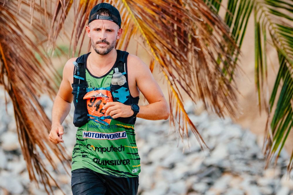 Runner in tank top participates in tropical beach race with palm trees in background.