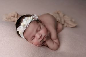 Sleeping newborn wearing delicate white floral headband posed on soft pink blanket in studio lighting.
