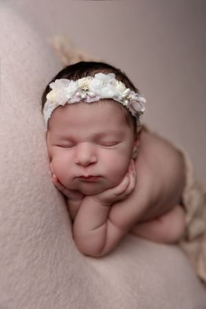 Sleeping newborn posed with delicate white floral headband on pink backdrop.