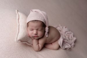 Sweet newborn sleeping on soft pink blanket wearing cozy knit hat in professional studio photo.