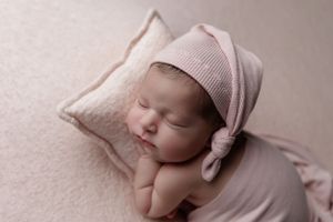 Peaceful newborn sleeping on pink pillow wearing soft knit bonnet.