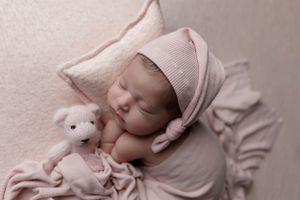Sleeping newborn in pink attire cuddles with small stuffed animal on soft blanket.