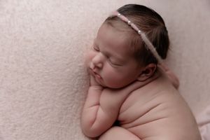 Peaceful newborn with delicate headband sleeps on pink textured background.