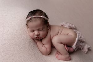 Peacefully sleeping newborn wearing delicate headband posed on soft beige backdrop in professional studio setting.
