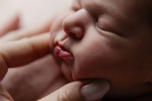 Close-up portrait of a sleeping newborn baby's face being gently touched by adult fingers.