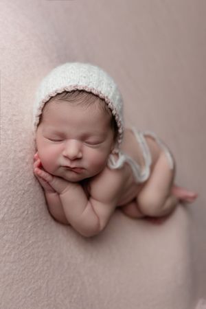 Sleeping newborn in white knit hat posed on pink background.
