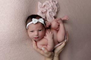 Newborn baby wearing white bow headband lying on pink fabric.