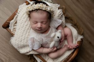 Sleeping newborn wrapped in cream blanket with tiny stuffed bunny in wooden basket.