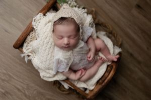Sleeping newborn wrapped in lace blanket resting in wooden basket.