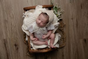 Sleeping newborn in white lace dress resting in vintage wooden basket with floral accents.