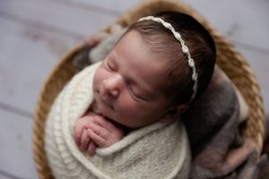 Peaceful newborn wearing white headband sleeps in round woven basket.