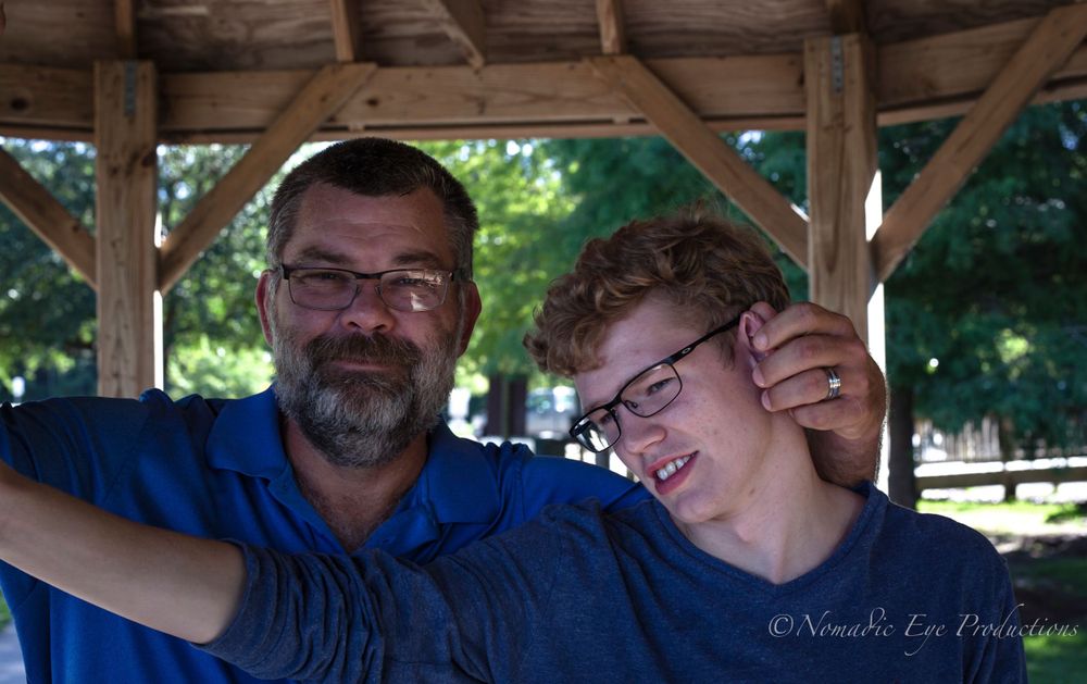 Two people sharing a tender moment under a wooden shelter outdoors.