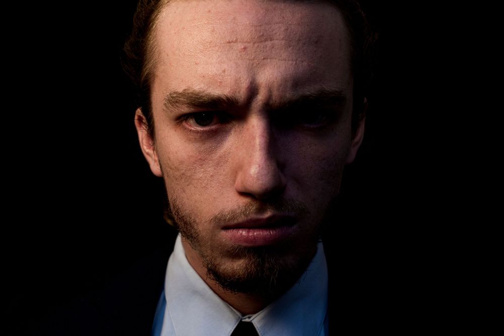 Moody low-key portrait with intense shadows highlighting facial features.