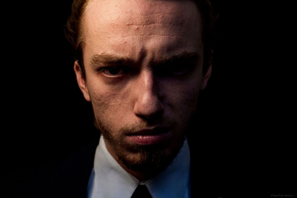 Dramatic low-key portrait of a person in business attire against dark background.