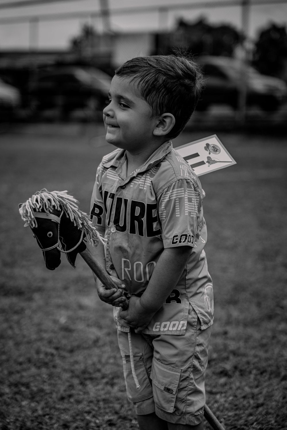 A child in sports uniform holds a lacrosse stick in black and white photography.