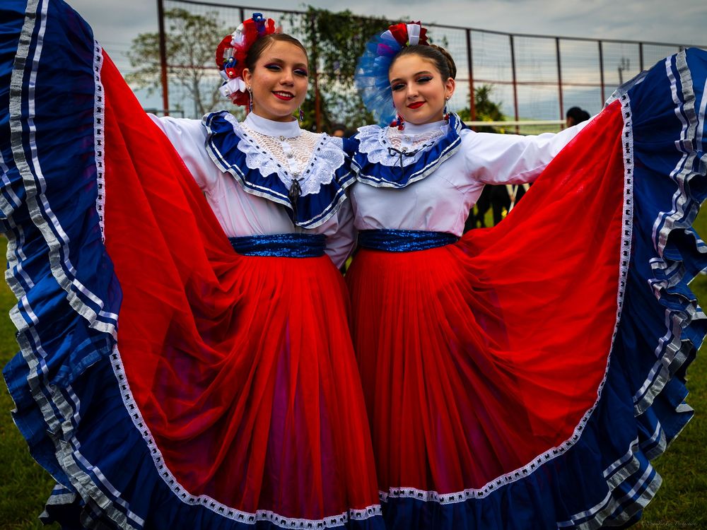 Folk dancers wearing traditional red and blue costumes pose with their flowing skirts spread wide.
