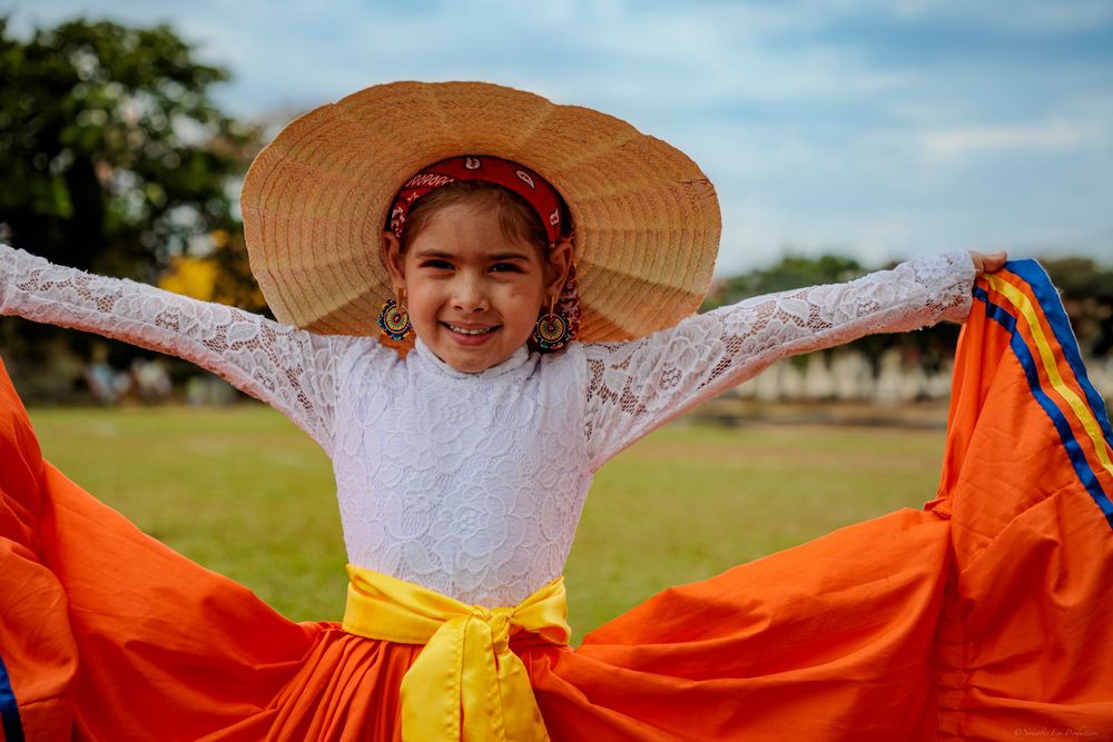 Joyful dancer in Mexican folk costume spreads orange skirt while performing in an outdoor setting.