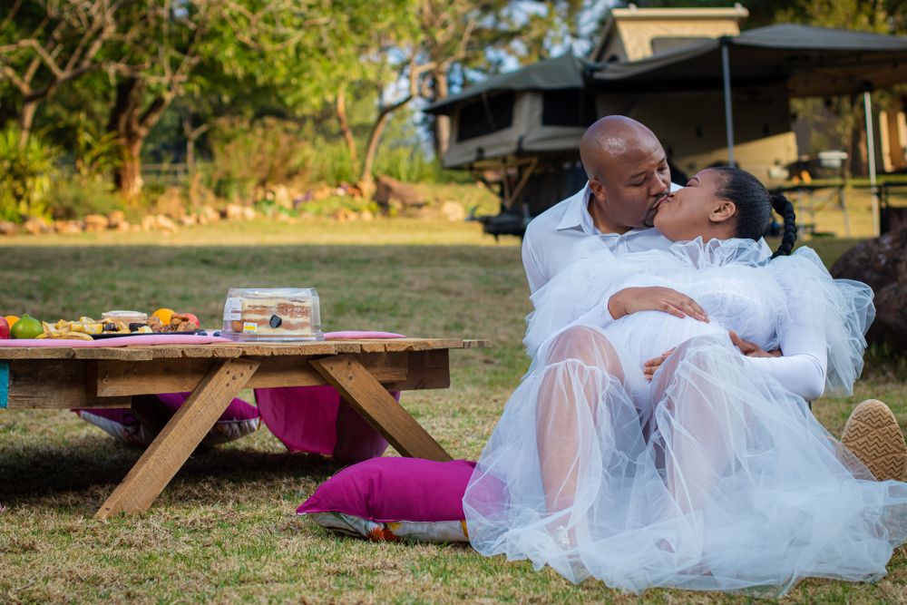 A couple sharing an intimate moment at an outdoor picnic with a wooden table and pink blanket.