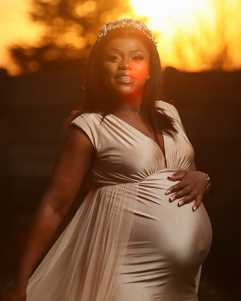 Maternity portrait in flowing white dress at sunset with golden lighting.