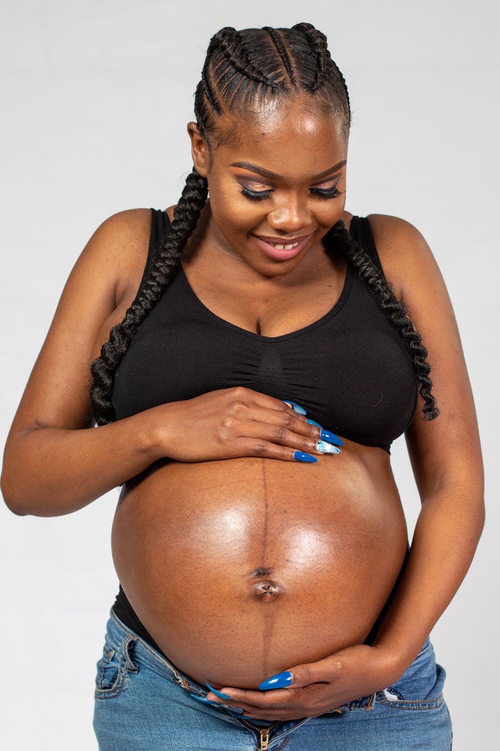 A pregnant woman in black top and jeans shows her baby bump in studio setting.