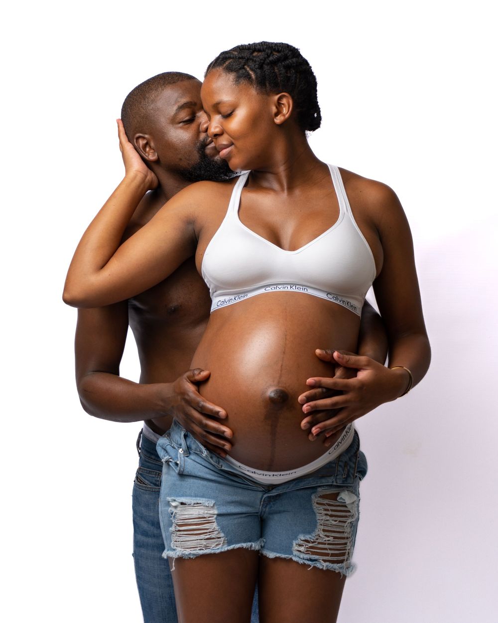 A loving maternity portrait features a couple in denim sharing an intimate moment.