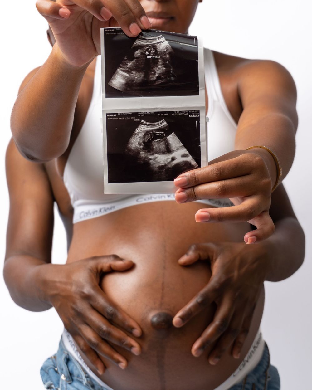 Hands hold ultrasound photos against a pregnant belly in an artistic black and white composition.