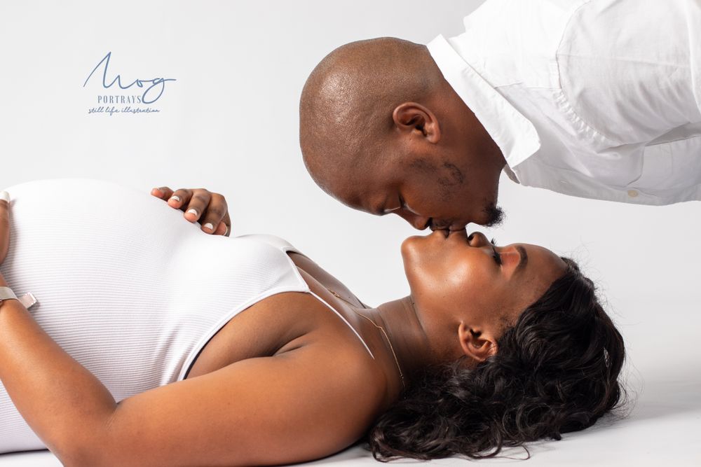 Artistic overhead maternity photo of couple in white creating intimate moment.