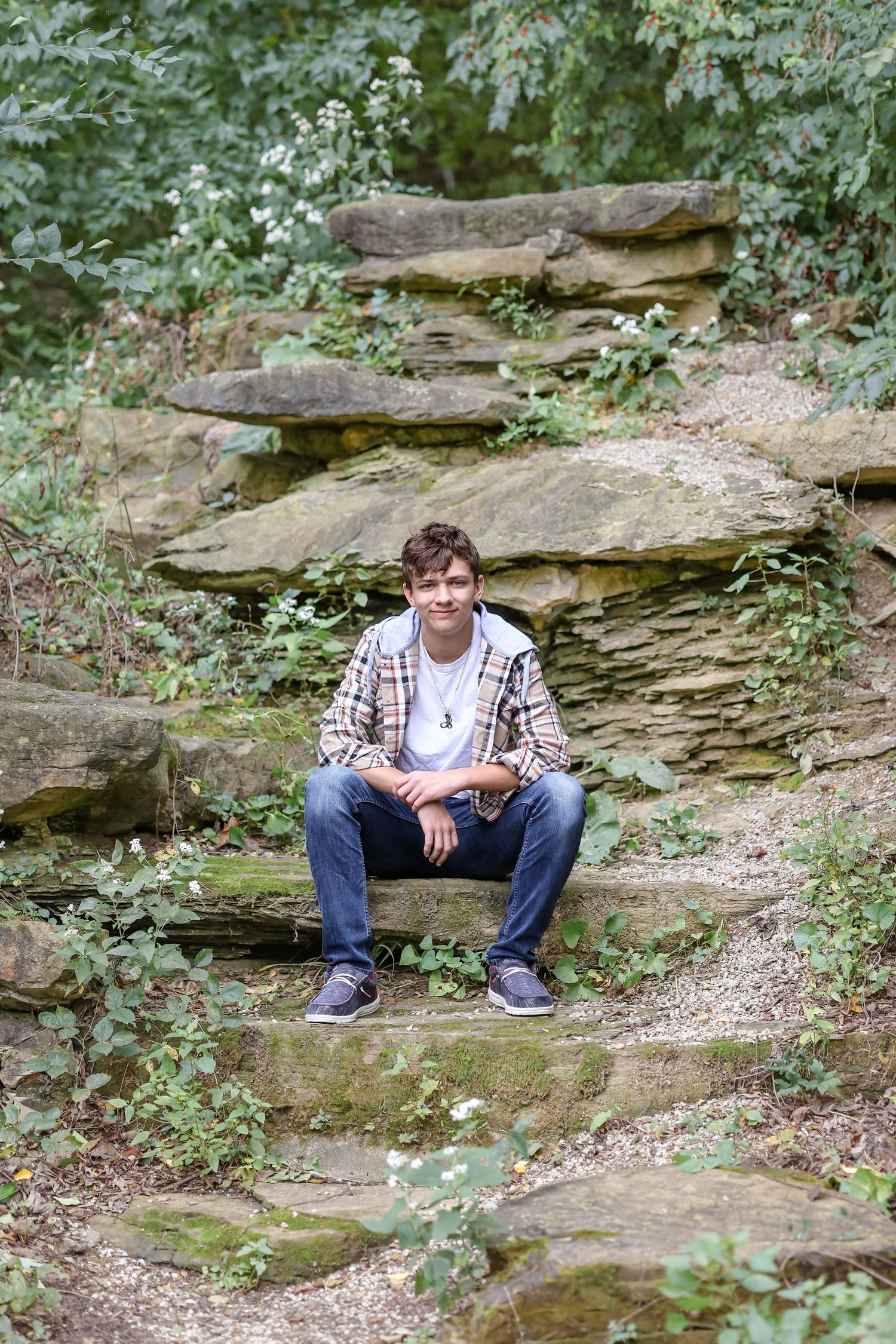 A relaxed outdoor portrait of someone sitting on natural rock formations surrounded by greenery.