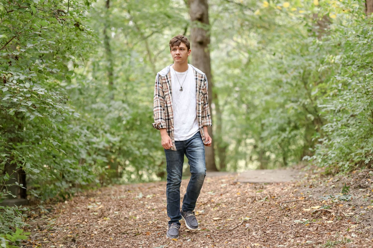 Casual portrait of person in plaid shirt standing on forest trail.