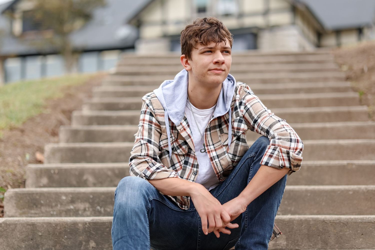 Person in casual plaid shirt sitting on concrete steps outdoors.