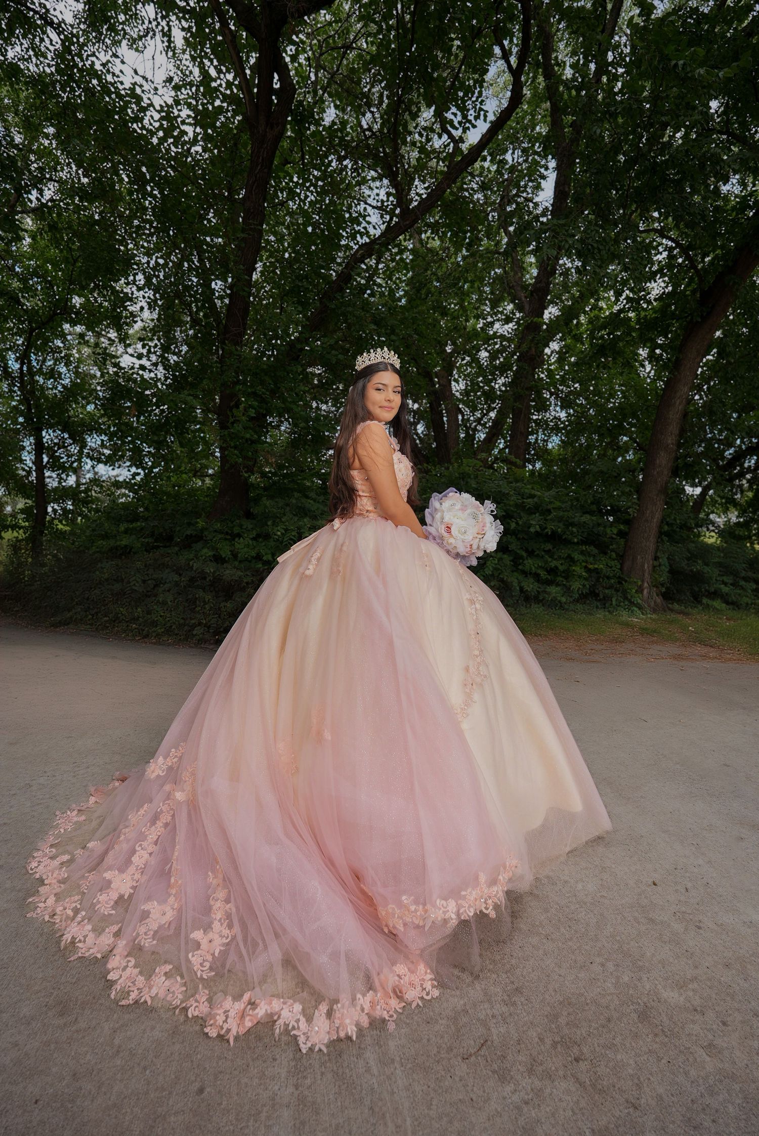 Stunning pink quinceañera dress with detailed lace trim photographed in a wooded setting.