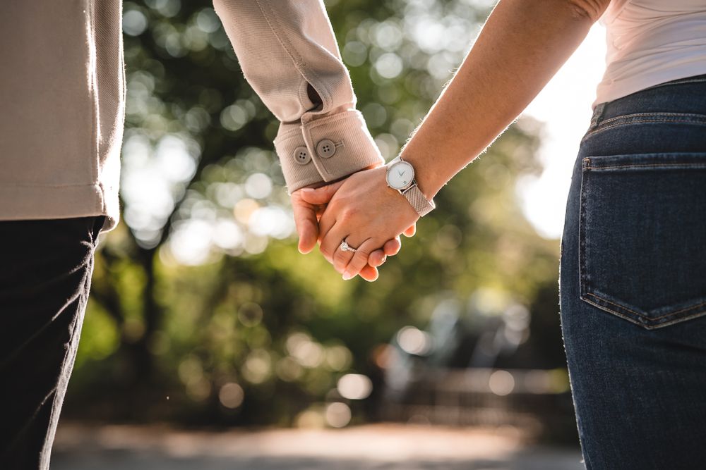 Close-up shot of two people holding hands outdoors.