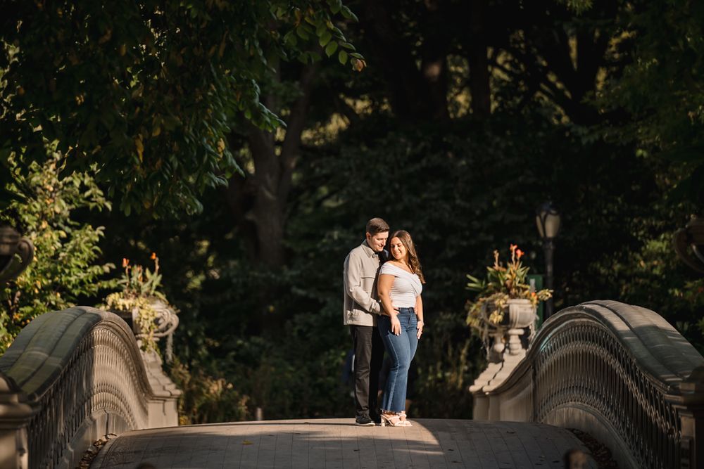 A romantic moment captured on a decorative stone bridge surrounded by lush green trees.