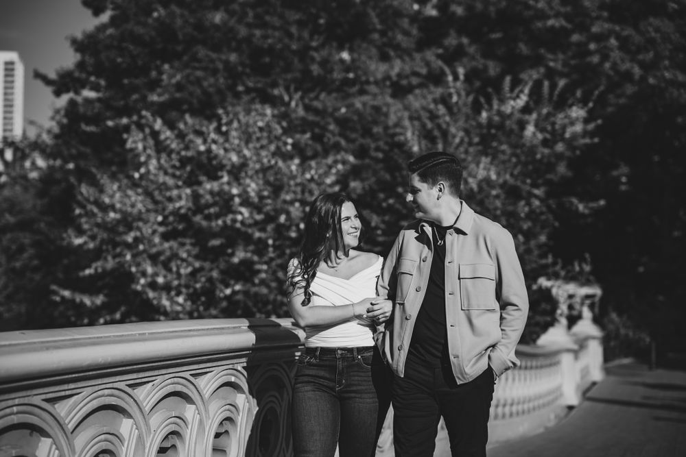 A black and white photo of a couple sharing a moment along an ornate stone bridge railing.