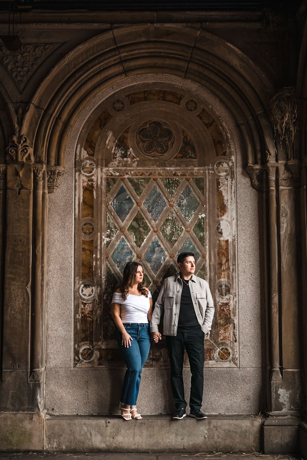 Couple standing against gothic stone architecture with decorative wall panels.