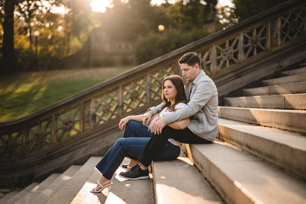 Couple sitting on stone steps during golden hour with sunlight filtering through trees.