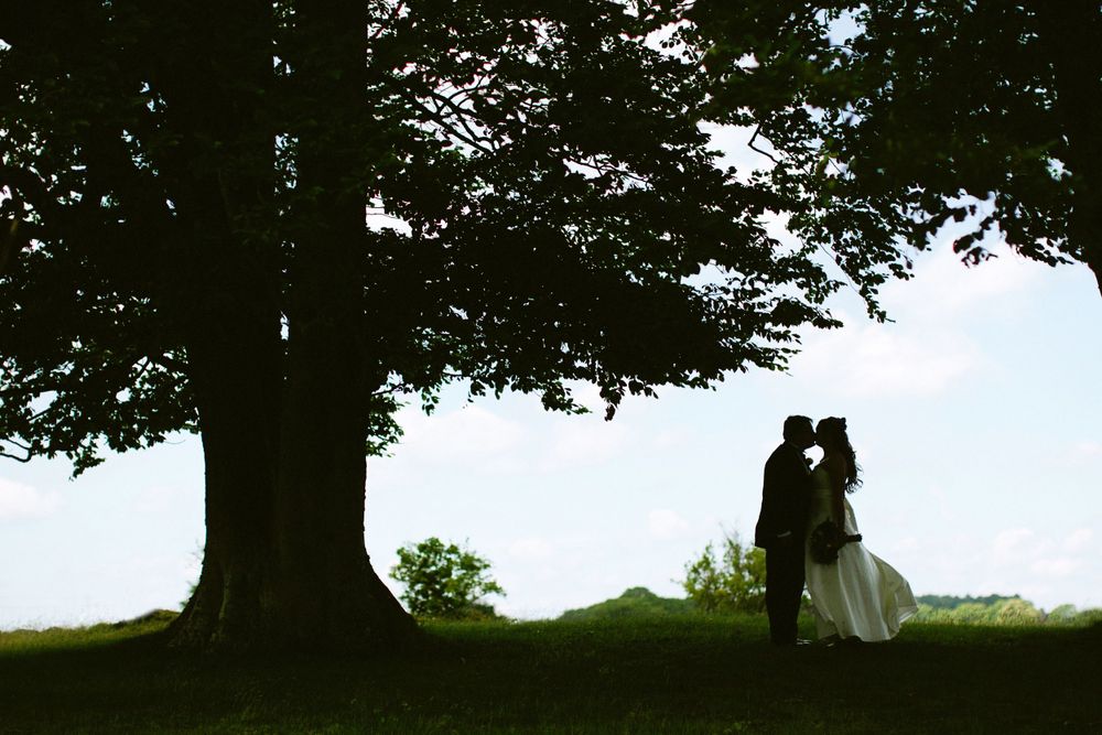 A romantic silhouette of a couple beneath a large tree on their wedding day.