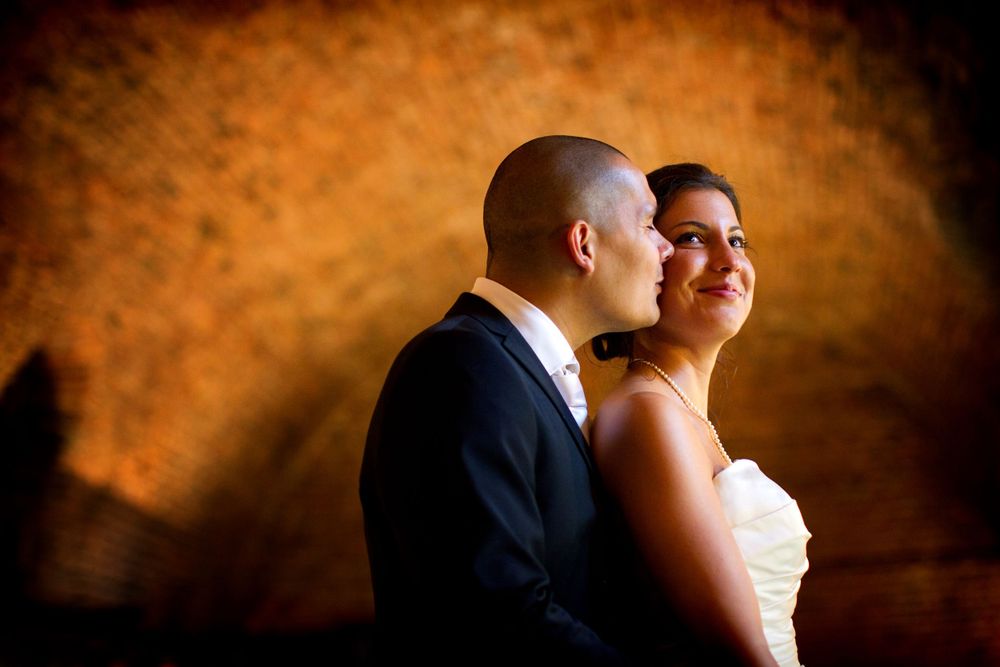 A romantic wedding portrait against a warm orange backdrop in dramatic lighting.